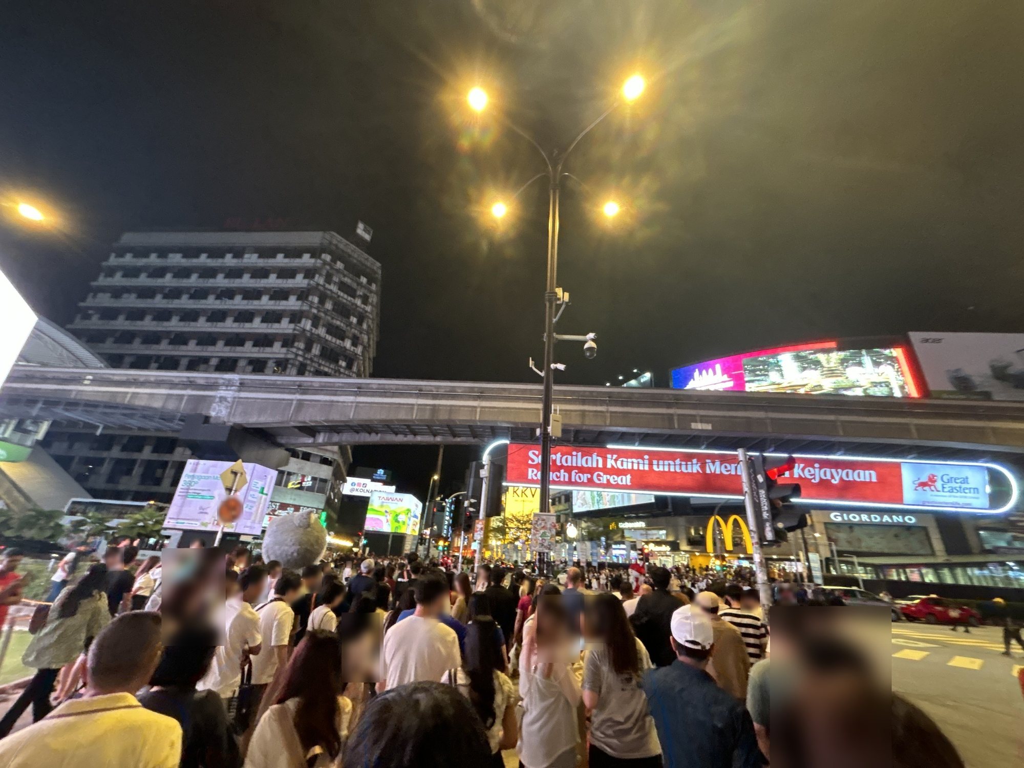 夜のブキッ・ビンタンの交差点を埋める人の波。頭上にモノレールの高架と電光看板