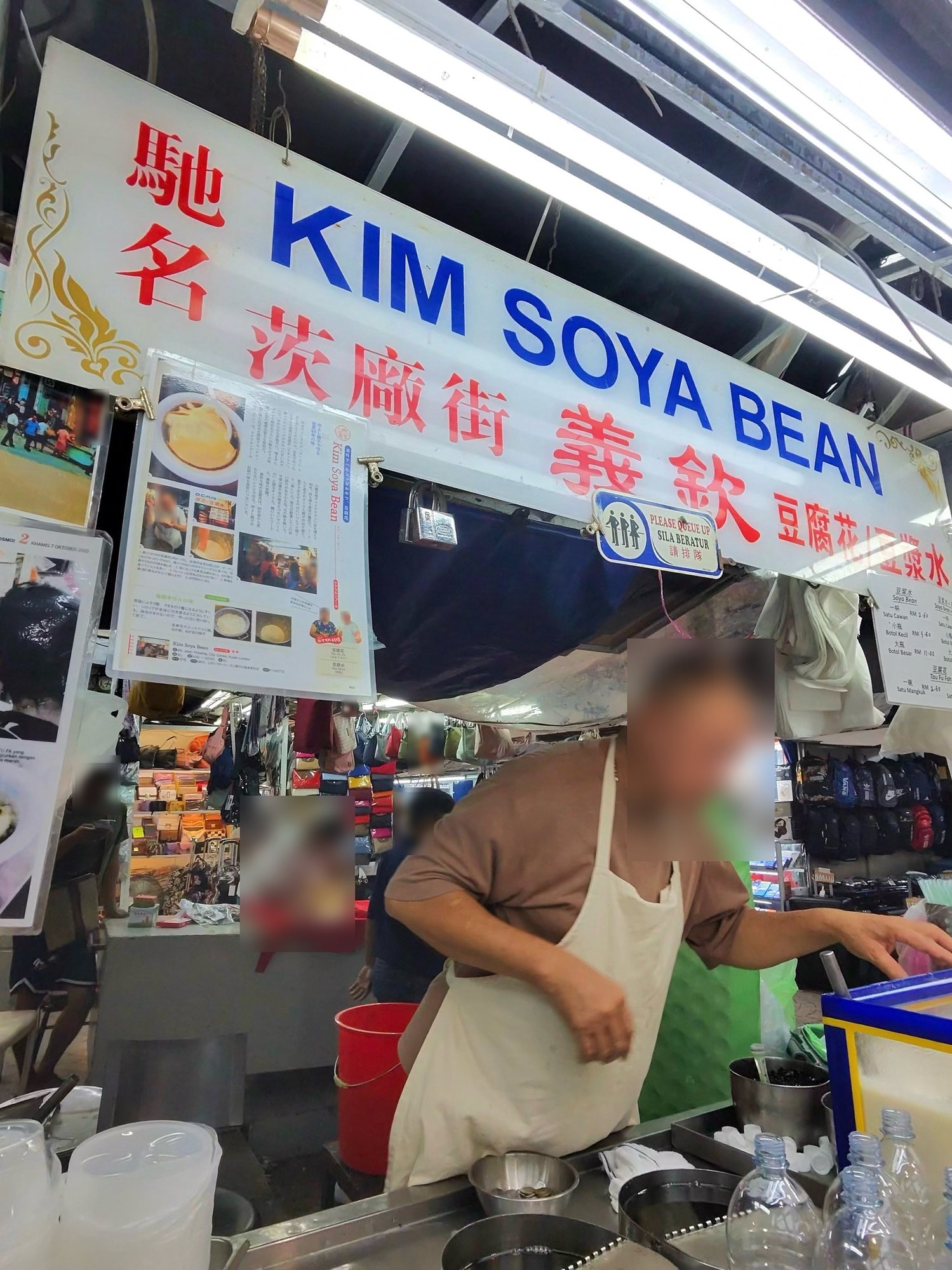プタリン通りの屋台「KIM SOYA BEAN」の看板の下で、白いエプロンの店の人が作っている