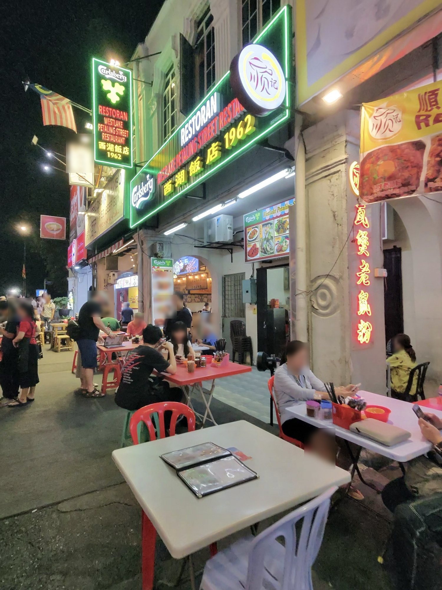 「西湖飯店 1962」の緑のネオンと、道に出した白と赤のテーブル