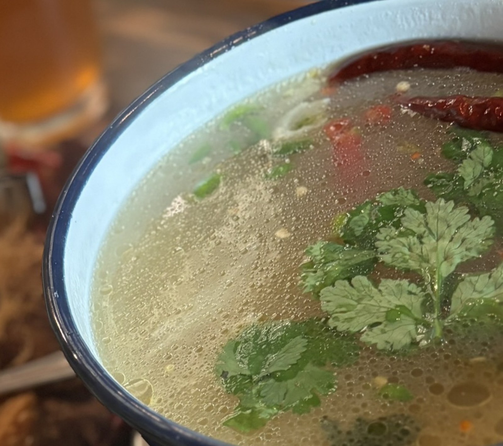 青い琺瑯鍋に入った澄んだ鶏のスープと丸ごとの乾燥唐辛子