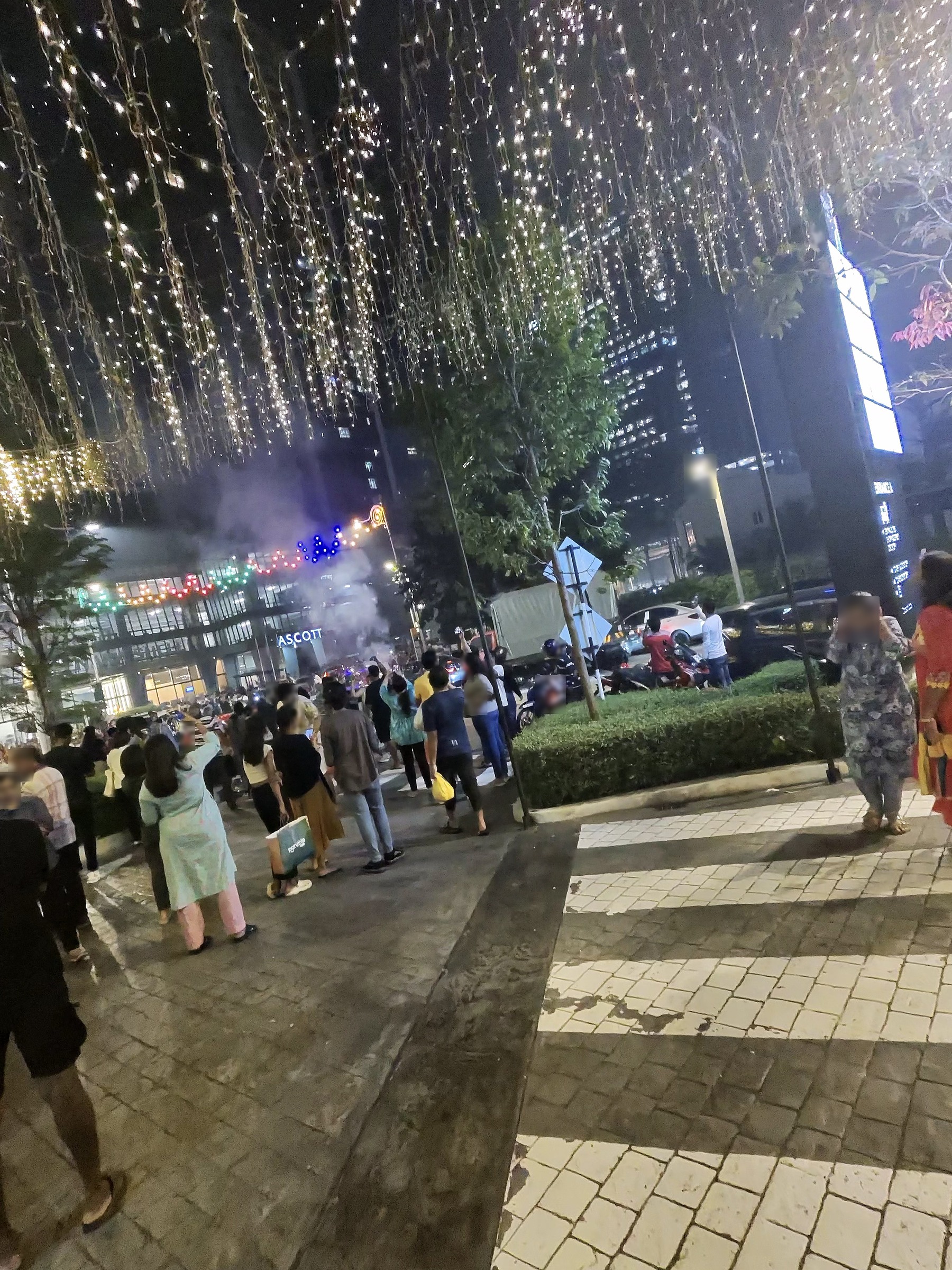 金色の電飾が垂れる並木道と、歩く人たち。奥にASCOTTの建物