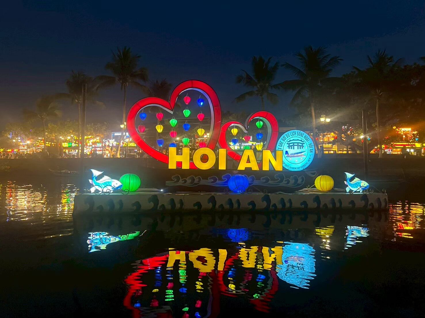 水辺の「HOI AN」のネオン看板と、水面に映った文字